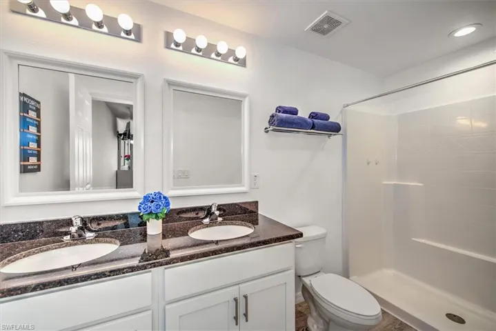 Bathroom featuring toilet, a sink, tiled shower, and visible vents