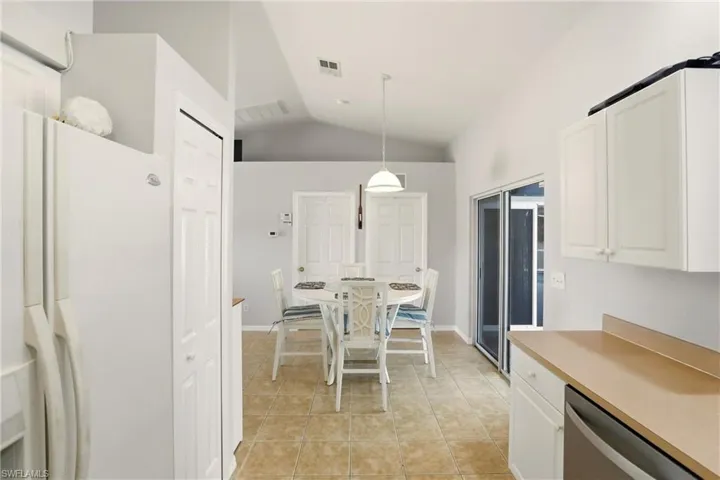 Kitchen with white fridge with ice dispenser, vaulted ceiling, white cabinetry, light countertops, and stainless steel dishwasher