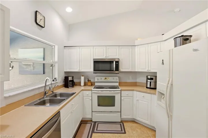 Kitchen featuring stainless steel appliances, white cabinetry, light countertops, light tile patterned flooring, and lofted ceiling