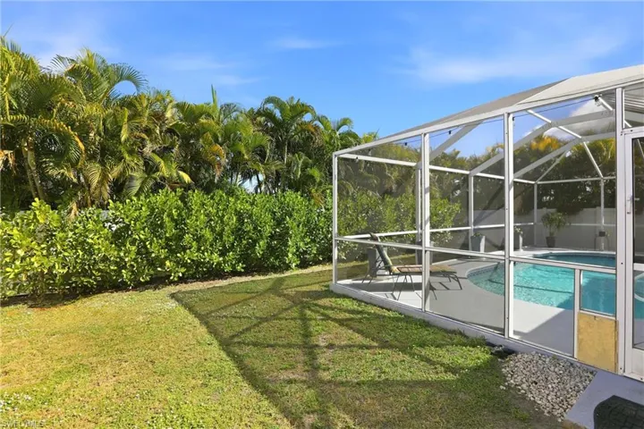 View of green lawn with a lanai, an outdoor pool, a sunroom, and a patio
