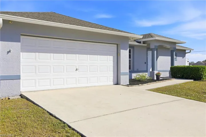 View of front of home with driveway, stucco siding, and roof with shingles