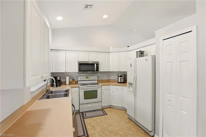 Kitchen featuring white appliances, white cabinetry, lofted ceiling, light countertops, and light tile patterned flooring