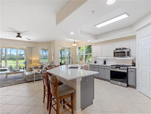 Kitchen with stainless steel appliances, gray and white cabinets, open floor plan, and light tile patterned floors