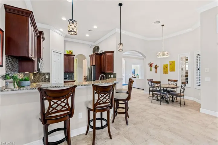 Kitchen featuring a chandelier, backsplash, arched walkways, light stone counters, and crown molding