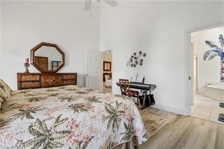 Bedroom with light wood-style flooring, a ceiling fan, a towering ceiling, and ensuite bath