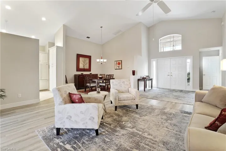 Living area with high vaulted ceiling, light wood-style flooring, a chandelier, and ceiling fan