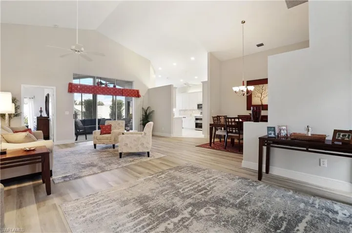 Living room with high vaulted ceiling, light wood-style flooring, a ceiling fan, and a chandelier