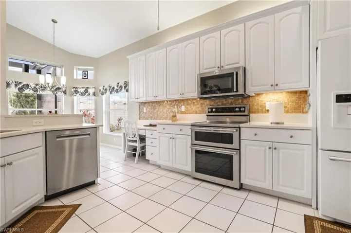 Kitchen featuring stainless steel appliances, white cabinets, hanging light fixtures, vaulted ceiling, and tasteful backsplash