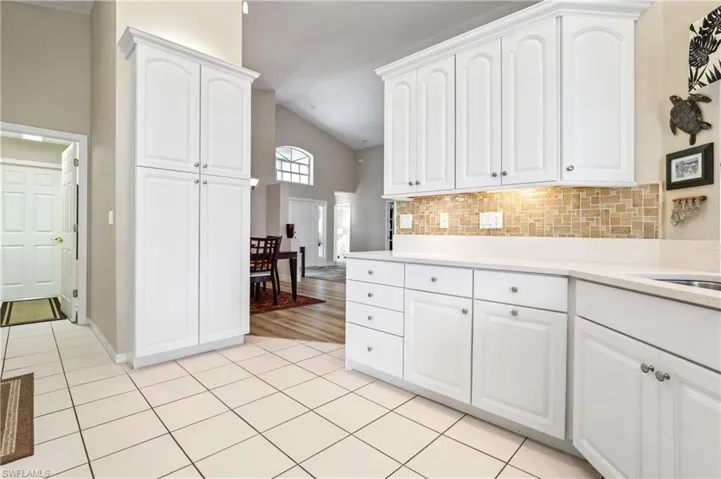Kitchen with white cabinetry, tasteful backsplash, light tile patterned floors, high vaulted ceiling, and light stone counters