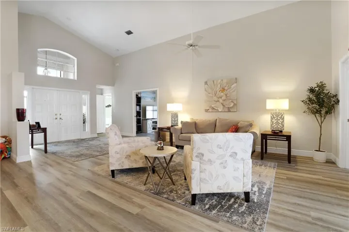 Living area with high vaulted ceiling, light wood-type flooring, a ceiling fan, and plenty of natural light