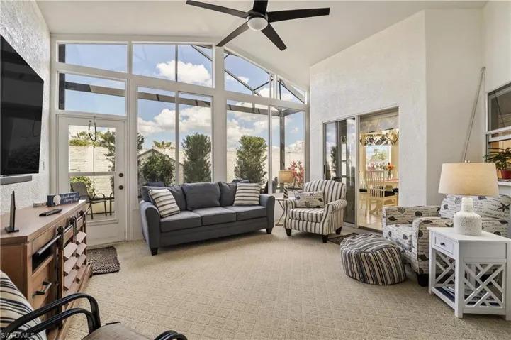 Sunroom / solarium with a textured wall, carpet floors, and high vaulted ceiling