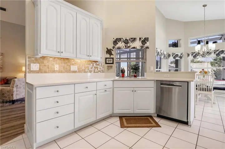Kitchen with high vaulted ceiling, white cabinets, stainless steel dishwasher, backsplash, and light tile patterned floors