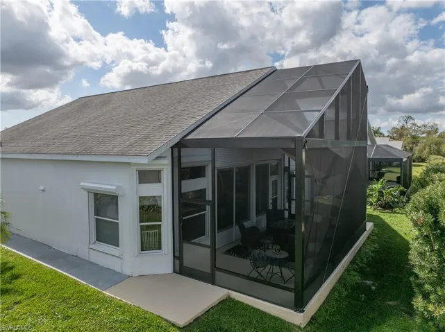 Rear view of house featuring a yard, roof with shingles, a sunroom, and stucco siding