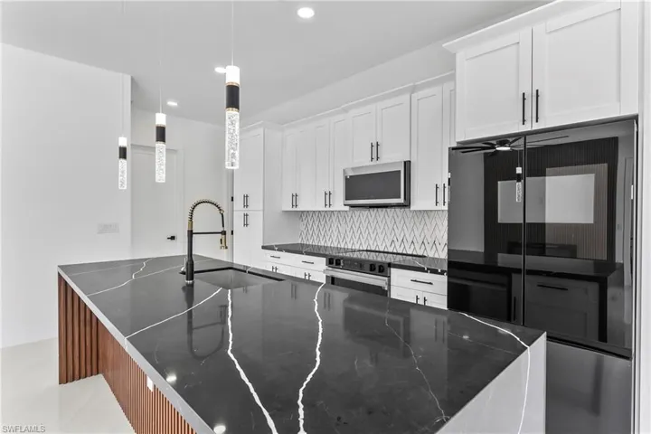 Kitchen with white cabinets, a kitchen island with sink, decorative backsplash, pendant lighting, and sink
