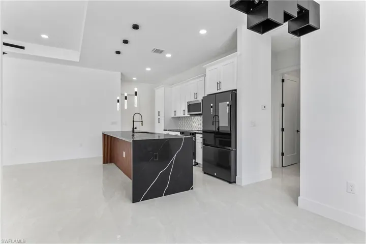 Kitchen with light tile patterned floors, white cabinets, a center island, black refrigerator, and pendant lighting