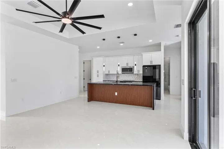 Kitchen with tasteful backsplash, a center island with sink, light tile patterned flooring, white cabinetry, and ceiling fan