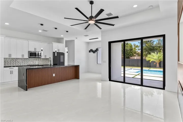 Kitchen with light tile patterned flooring, white cabinetry, black fridge, and a center island with sink