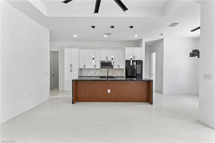 Kitchen with tasteful backsplash, light tile patterned floors, black refrigerator, ceiling fan, and a center island with sink