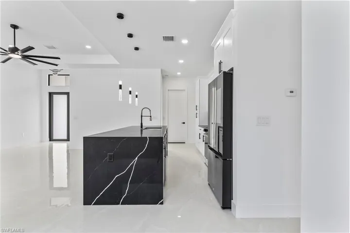 Kitchen with white cabinets, sink, hanging light fixtures, stainless steel refrigerator, and ceiling fan