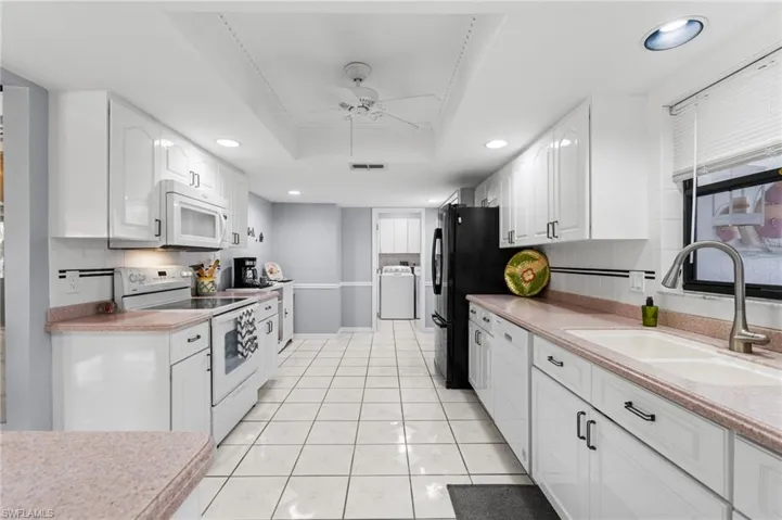 Kitchen featuring white appliances, white cabinets, sink, a tray ceiling, and washer / dryer