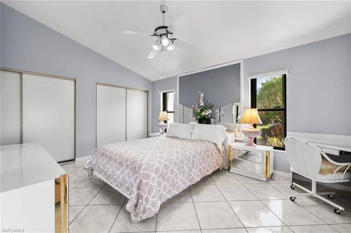 Bedroom with light tile patterned floors, two closets, vaulted ceiling, and ceiling fan