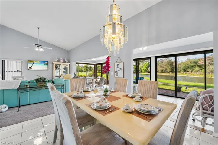 Dining space featuring light tile patterned floors, ceiling fan with notable chandelier, and high vaulted ceiling