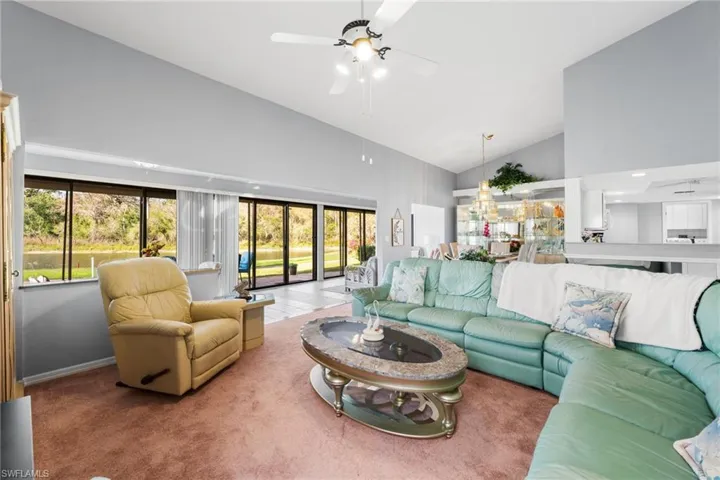 Carpeted living room featuring ceiling fan, high vaulted ceiling, and a healthy amount of sunlight