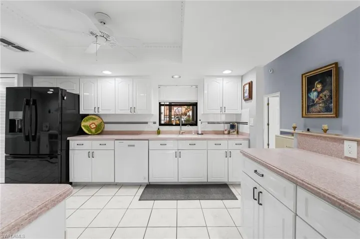 Kitchen with black fridge with ice dispenser, white dishwasher, a raised ceiling, and white cabinetry
