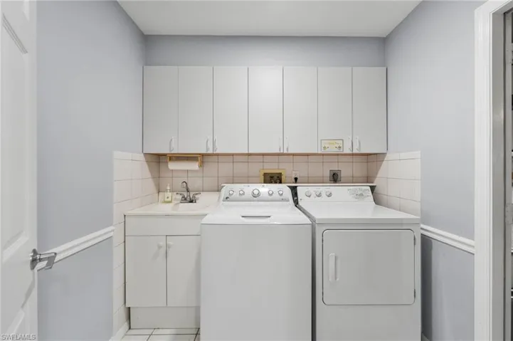 Laundry area with separate washer and dryer, sink, light tile patterned floors, and cabinets