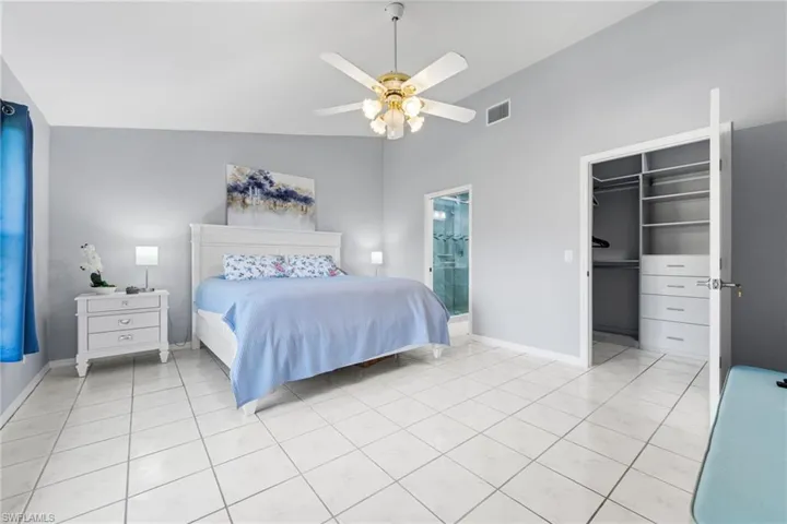 Tiled bedroom with a walk in closet, ensuite bath, ceiling fan, a closet, and lofted ceiling