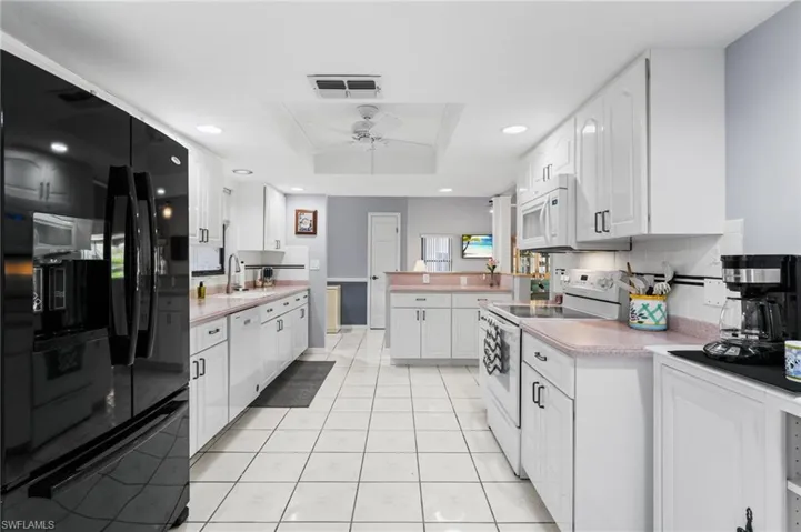 Kitchen featuring white appliances, a raised ceiling, sink, ceiling fan, and white cabinetry