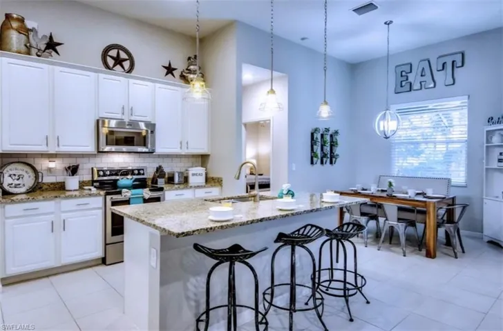 Kitchen with stainless steel appliances, light stone countertops, a kitchen island with sink, white cabinets, and decorative backsplash