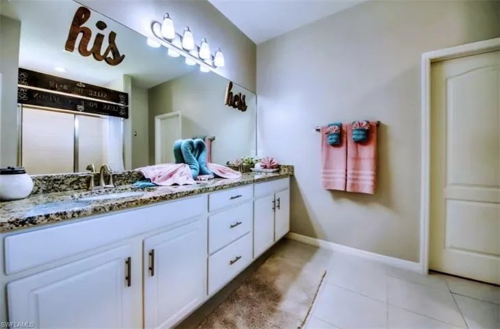 Bathroom featuring light tile patterned flooring, double vanity, and a shower