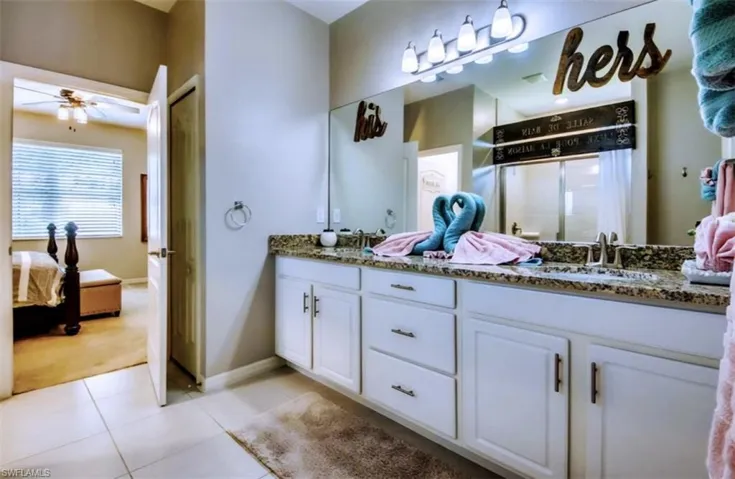 Ensuite bathroom featuring double vanity, light tile patterned floors, a shower stall, and a ceiling fan