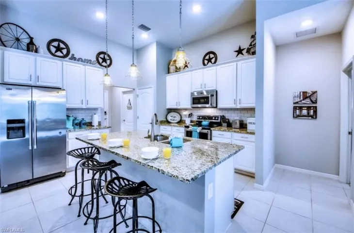 Kitchen featuring stainless steel appliances, light stone counters, tasteful backsplash, and white cabinets