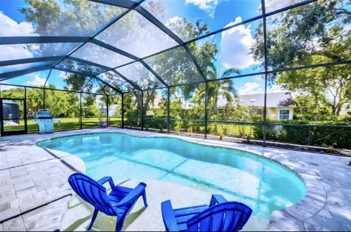 Outdoor pool featuring glass enclosure, grilling area, a sunroom, and a patio area