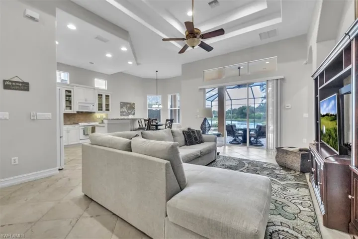 Living area with a ceiling fan, a towering ceiling, plenty of natural light, light tile patterned floors, and a tray ceiling
