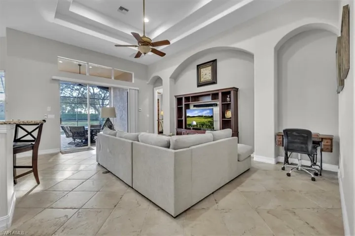 Living room with arched walkways, a desk, a ceiling fan, a raised ceiling, and a towering ceiling