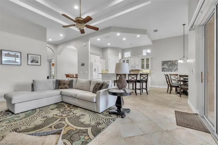 Living room featuring arched walkways, recessed lighting, ceiling fan, light tile patterned flooring, and a raised ceiling