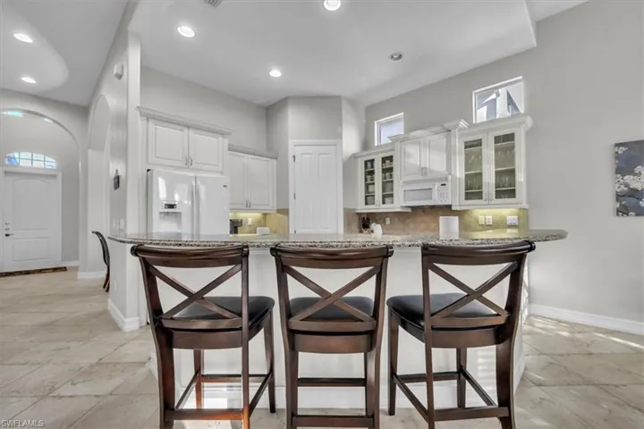 Kitchen with glass insert cabinets, a breakfast bar area, white appliances, light stone counters, and white cabinetry