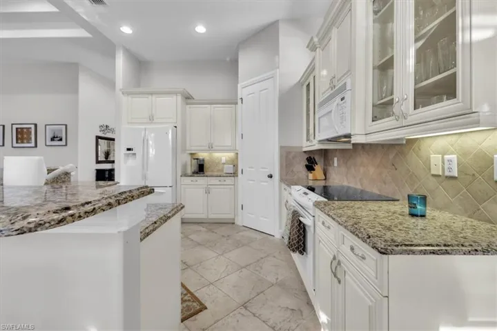Kitchen with light stone countertops, white appliances, glass insert cabinets, decorative backsplash, and recessed lighting