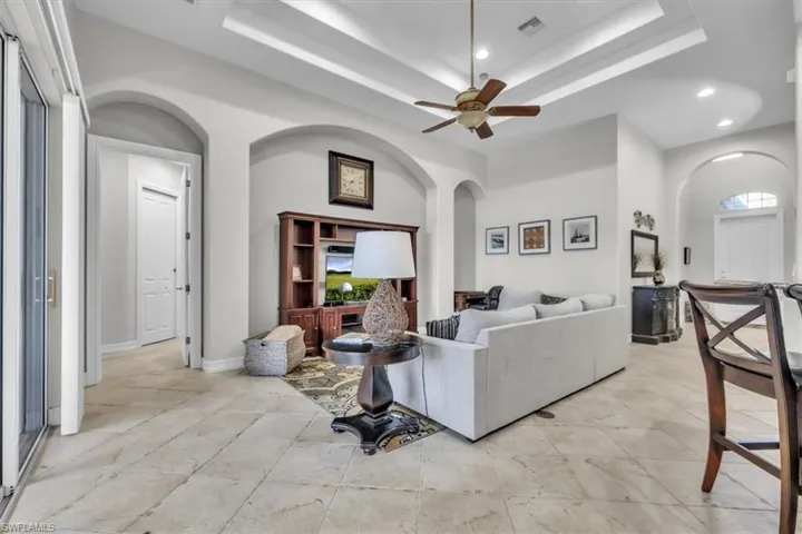 Living room with arched walkways, a ceiling fan, recessed lighting, and a raised ceiling