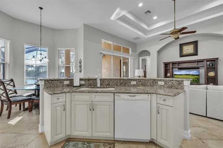Kitchen featuring white cabinets, open floor plan, dishwasher, light stone countertops, and a kitchen island with sink