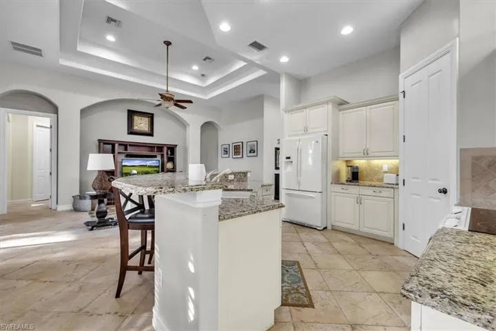 Kitchen with arched walkways, a breakfast bar, light stone countertops, white refrigerator with ice dispenser, and decorative backsplash