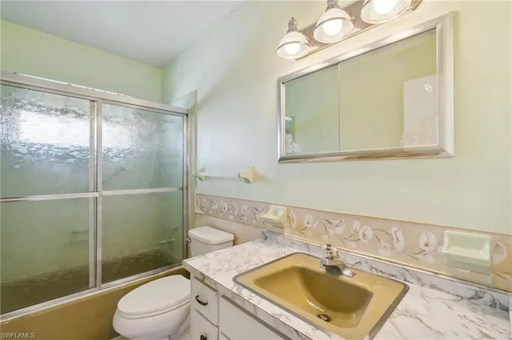 Bathroom featuring vanity, combined bath / shower with glass door, and decorative backsplash