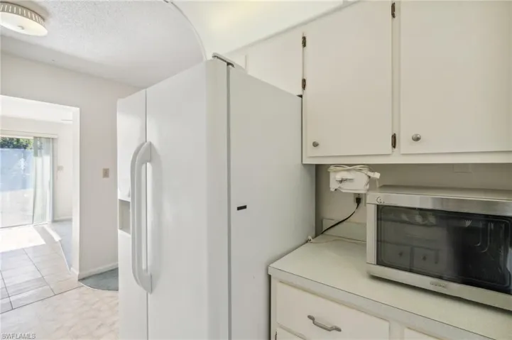 Kitchen with white fridge with ice dispenser, stainless steel microwave, white cabinets, and light countertops