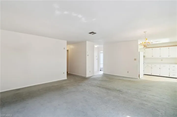 Unfurnished living room with light carpet and a chandelier