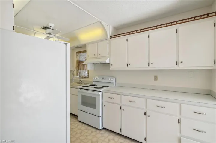 Kitchen featuring white appliances, light countertops, white cabinets, light flooring, and a ceiling fan