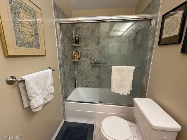 Bathroom with toilet and shower / bath combination with glass door