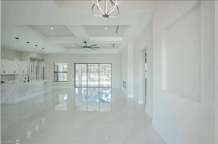 Empty room with coffered ceiling, sink, ceiling fan with notable chandelier, and beam ceiling